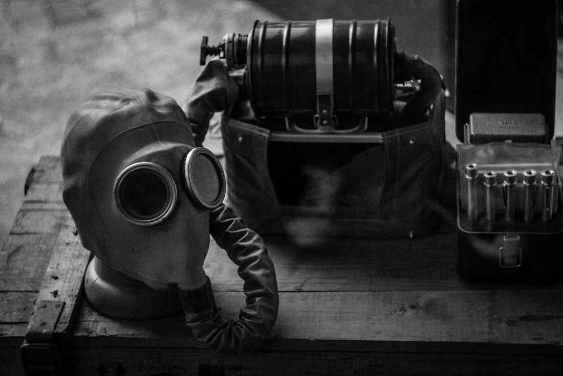 Vintage gas mask with breathing hose, filtration device, and ammunition box on a wooden crate in black and white.