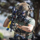 A 3/4 shot of a man wearing tactical gear, helmet, night vision goggles with a CM-8M gas mask, while holding an AK-47 rifle.